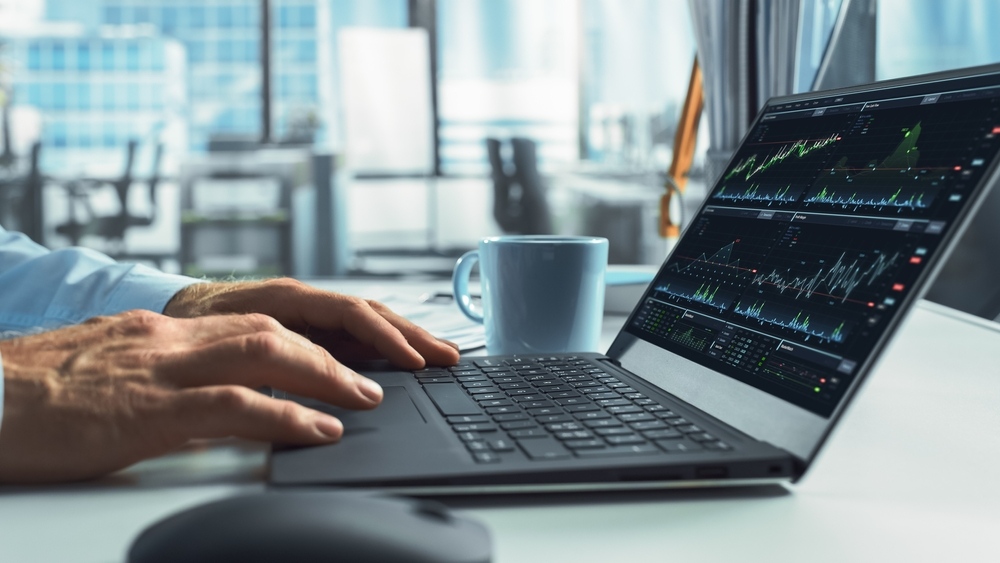 Person reviewing stock market charts on a laptop in a modern office
