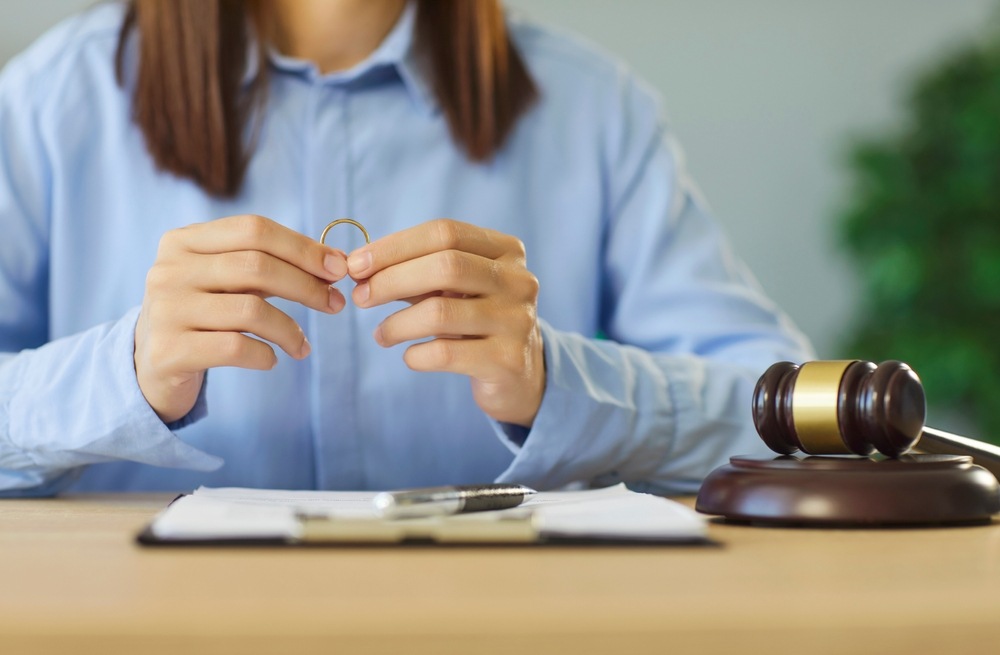Woman holding her wedding ring above divorce paperwork next to a judge's gavel